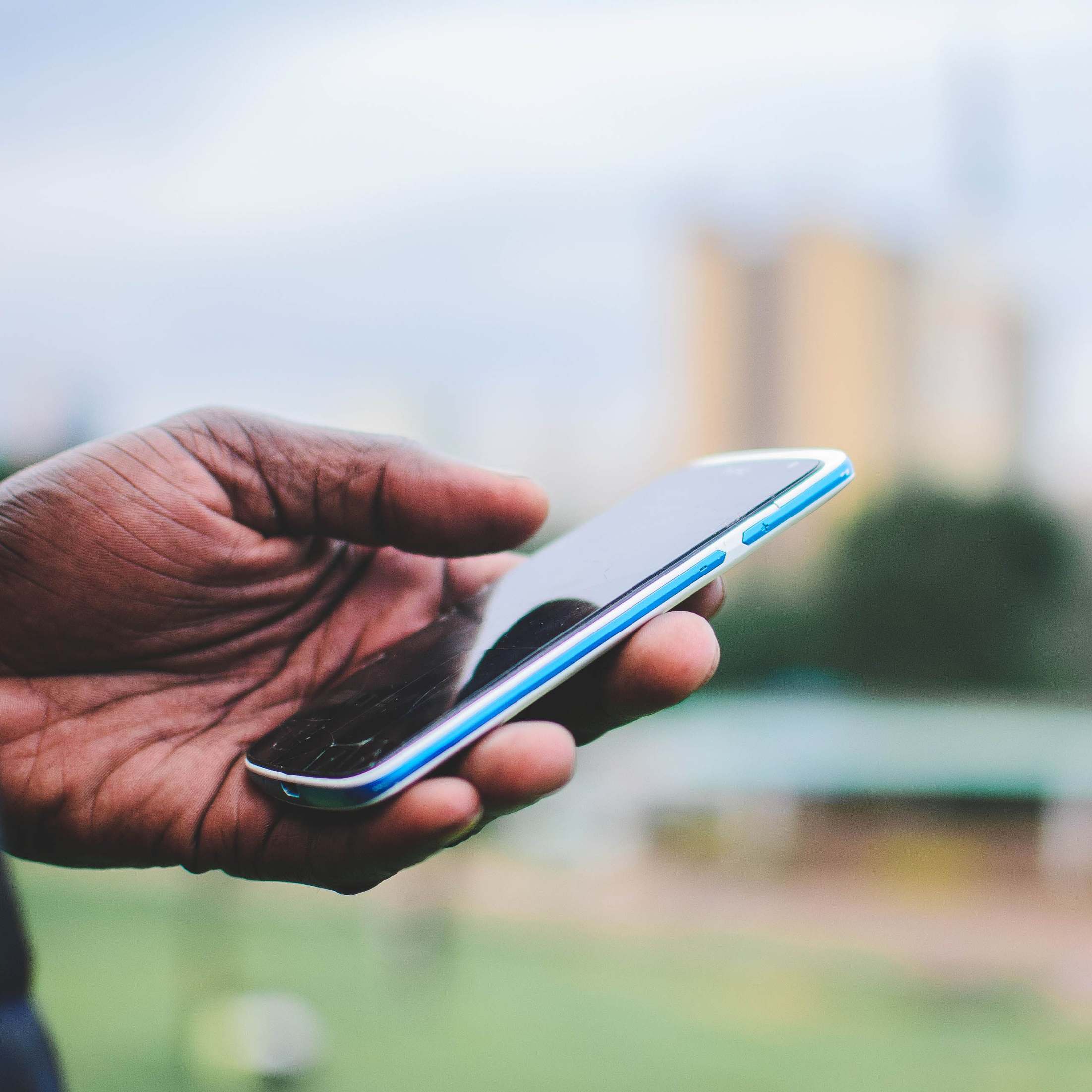 Hands holding a smartphone showing a secure application screen, close-up of a hand holding a smartphone with blurred urban background